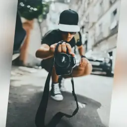Mężczyzna w czapce z daszkiem trzyma aparat, gotowy do uchwycenia chwili. Jego zawód to fotograf.