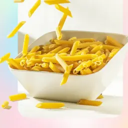 Penne spadające do białej miski, uchwycone przez fotografa jedzenia.
