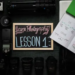 Zestaw sprzętu fotograficznego i tablica z napisem "Learn Photography LESSON 1" – idealny na kurs fotografii dla początkujących.