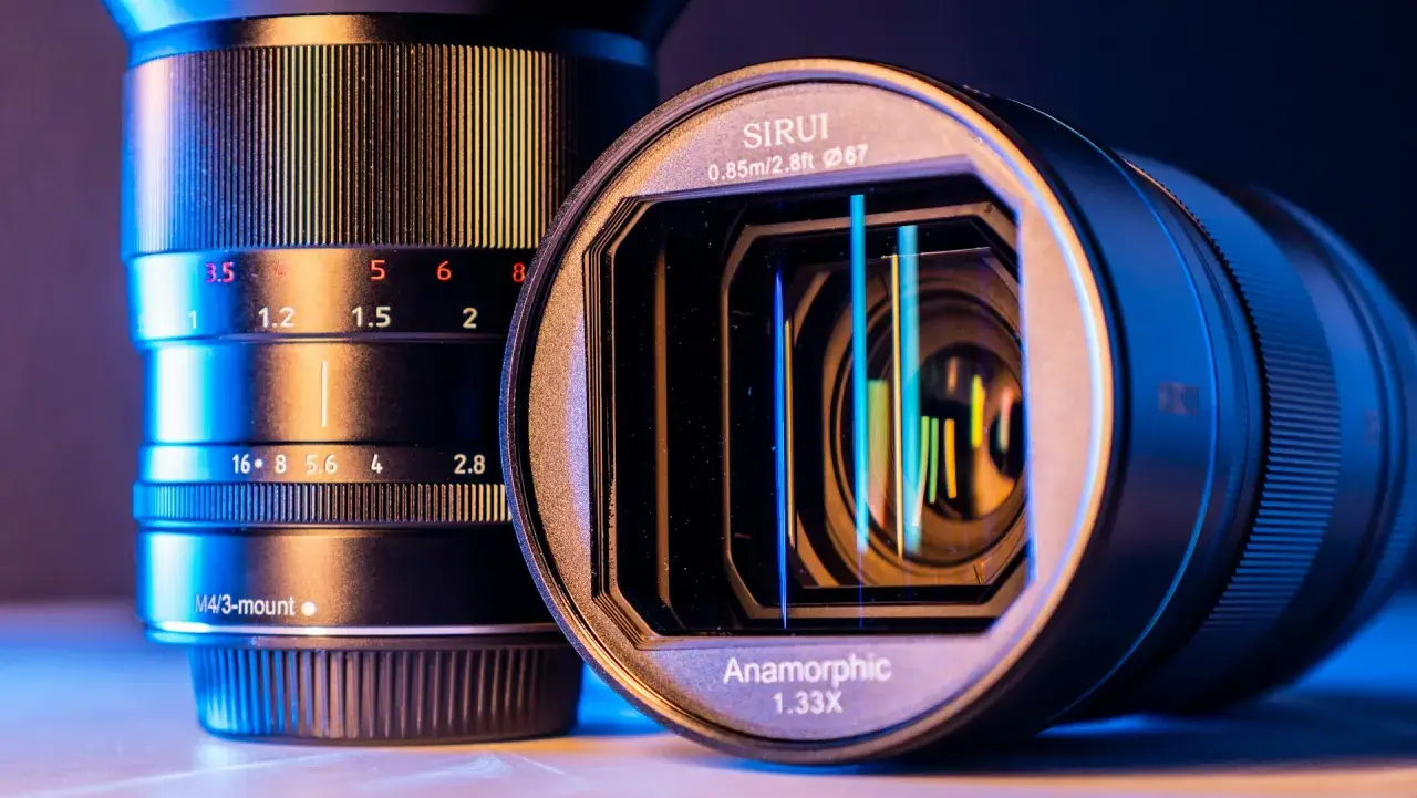 Dwa obiektywy, jeden z oznaczeniami przysłony, drugi z napisem "Anamorphic 1.33X", oświetlone niebieskim i żółtym światłem.